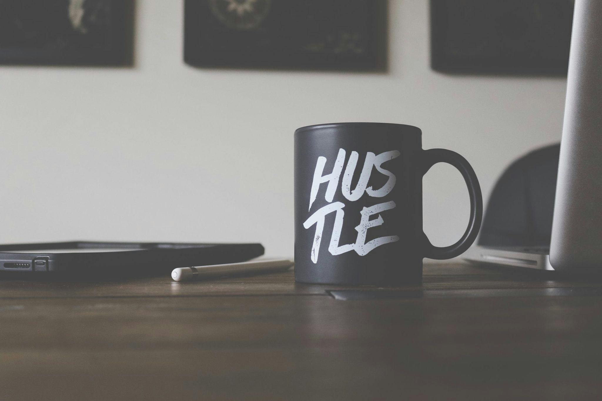 A black mug with white writing that says "hustle" on a coffee table