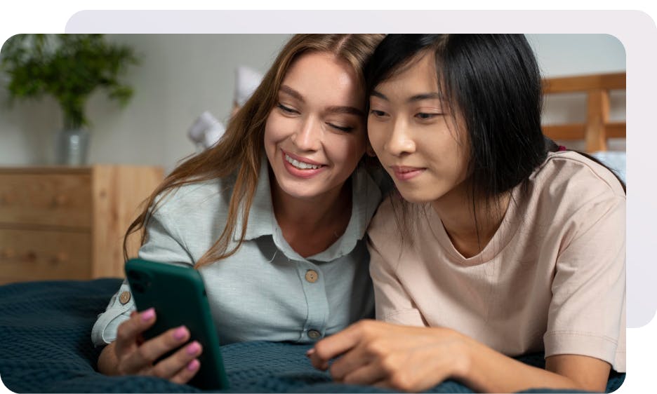 two girls sitting down and smiling at a phone 