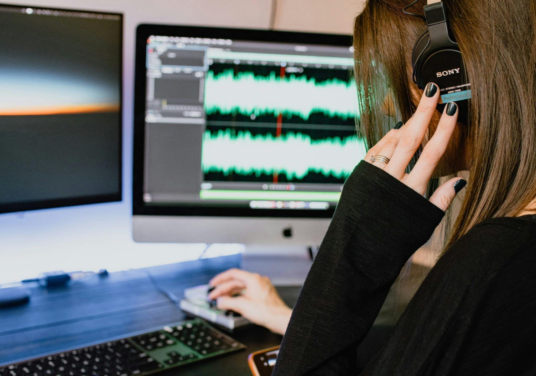 A woman wearing headphones editing her audio brand on computer screen